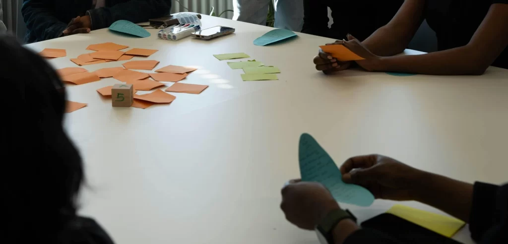 Equipe de profissionais participando de uma reunião para aprender como fazer o plano de negócio perfeito para sua empresa, usando notas adesivas de cores diferentes para organização.
