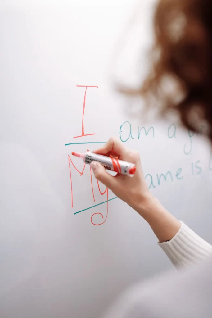 Melhor Custo Benefício Curso de Inglês: Guia Completo (Economia: Pessoa com caneta marcador escreve números e letras na lousa branca, com rascunhos em vermelho e azul, em ambiente claro de estudo e aprendizado de inglês.